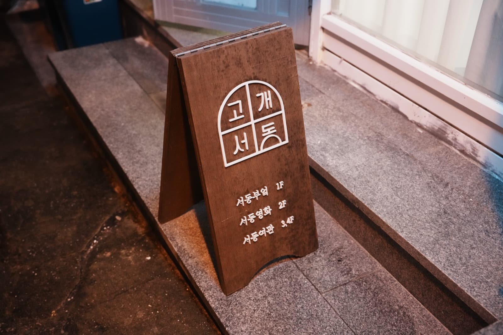 돌계단 위 나무 입간판. 고개서동 로고 아래 층마다 공간 이름이 적혀 있다.